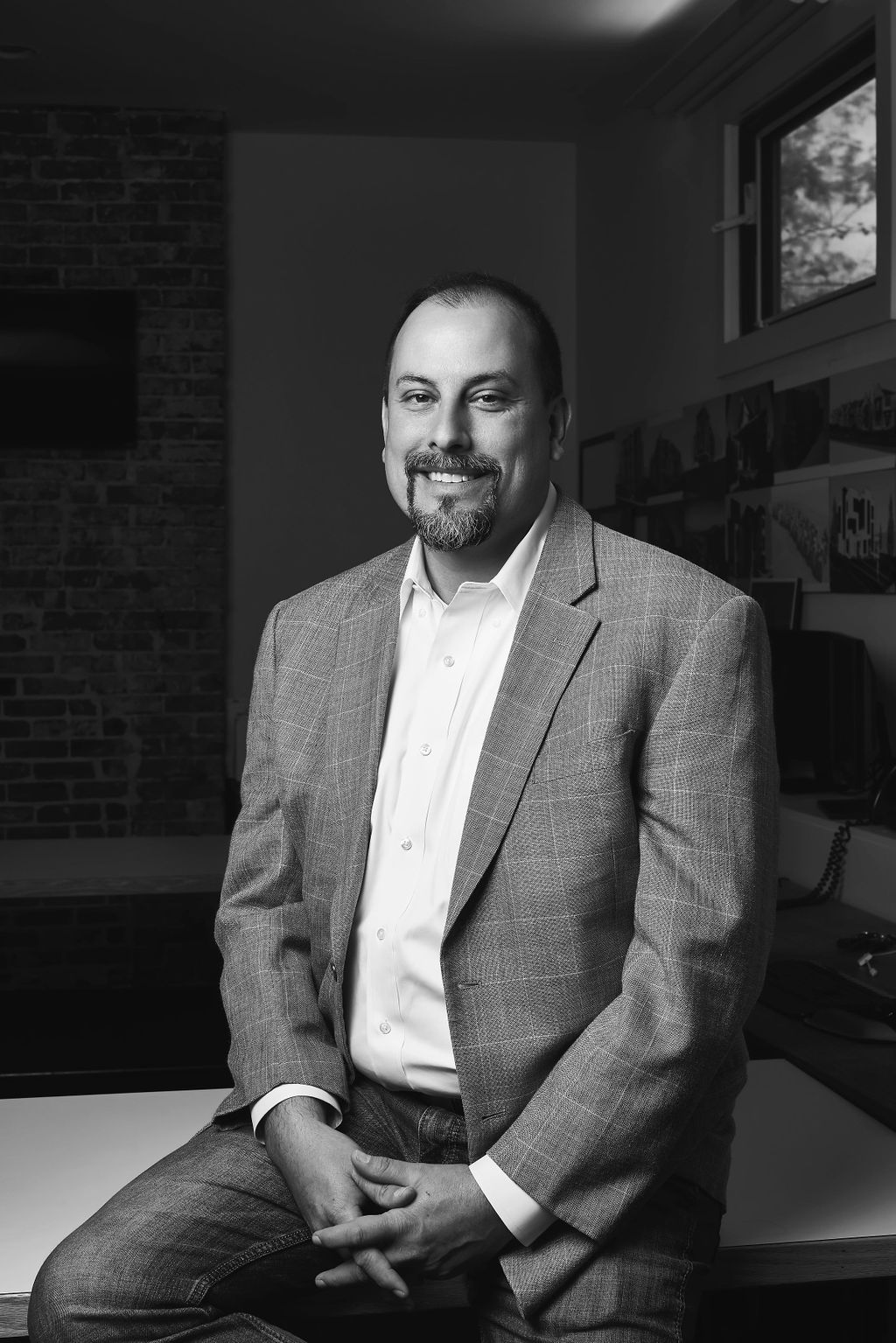 Portrait of John E. Root, AIA, (circa 2018) a seasoned AIA and NCARB state licensed Architect, take in front of a backdrop of architectural designs he displays inside his office in Nashville, TN. He is wearing professional attire and exudes a sense of professionalism, creativity and expertise.